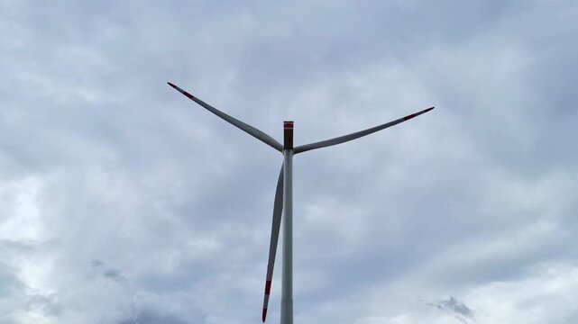 Mainz, Rhineland-Palatinate, Germany: Close up view of modern wind turbine rotating beneath dramatic cloudy sky highlighting renewable energy