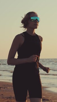 Sporty woman running on beach at sunset in black sportswear. Healthy lifestyle, cardio workout