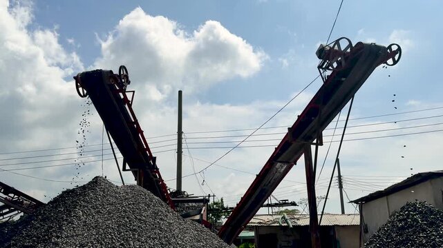 Industrial gravel conveyor belts in operation under a bright blue sky with scattered clouds