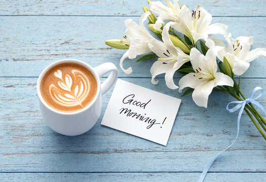 Beautiful white lilies with a hot latte and good morning card on rustic table