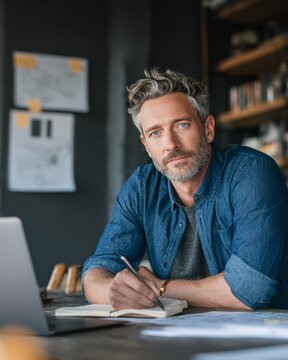 Mature man writing notes at desk during hybrid work meeting