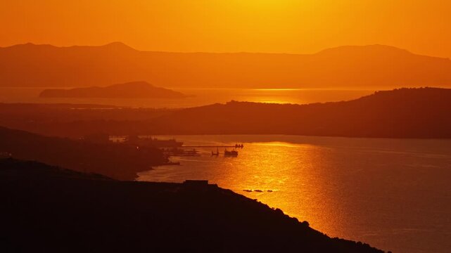 Aerial drone view of a large enclosed natural harbor bay at sunset with hills fading into a golden haze, Chania, Greece