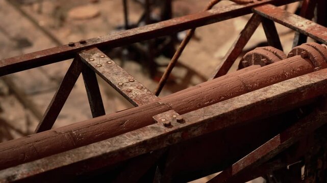 A construction site shows a close view of a metal framework and a wooden beam. Tools and materials are scattered around. The area appears to be busy with ongoing work.