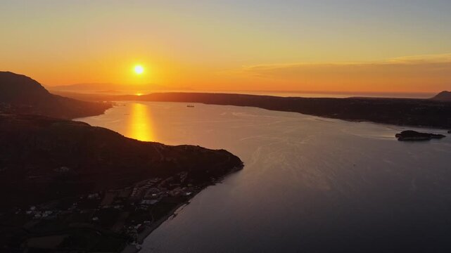 Aerial drone view of a wide bay and coastal resort town below a long headland at sunset, Chania, Greece