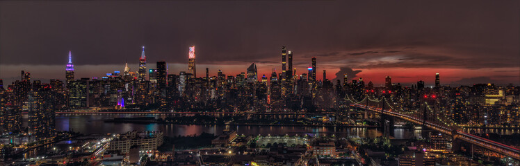 Fototapeta premium A dazzling night view of New York City skyline, showcasing iconic skyscrapers illuminated against a dramatic sunset. The scene highlights the vibrant urban lights and picturesque reflections.