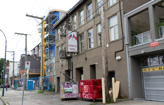 The American Hotel's sign with crossed American and Canadian flags juts over a Main Street sidewalk in the Downtown Eastside, scaffolding rising next door.