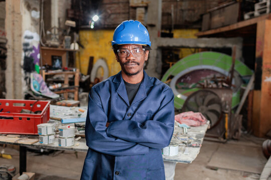 A worker stands in a busy workshop wearing a blue helmet and glasses