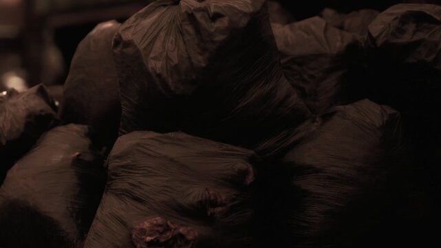 Several black waste bags are piled up in a dimly lit area. The cleaning work has finished, leaving bags ready for disposal. The setting suggests a cleanup project during evening hours.
