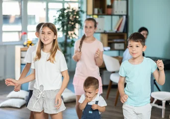 Children actively jump and dance during music lesson, teacher accompanies on piano in kindergarten, music lesson... © JackF