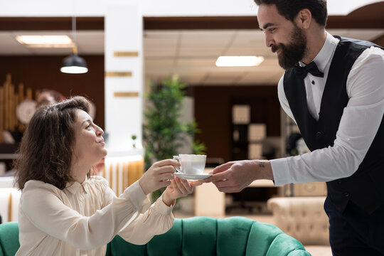 Hotel manager with coffee cup coordinates bellhop and hotel staff, representing luxury resort service and efficient hospitality operations.