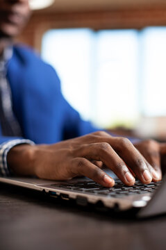 Hands of startup employee on keyboard, working on laptop at modern desk, closeup of black man typing on digital device to update financial analysis data for company project in office.