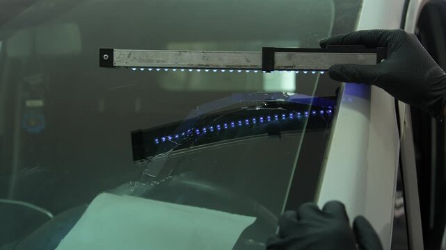 Windshield UV Resin Curing 4k video. Windshield repair. Automotive technician holds ultraviolet lamp over broken car glass. Mechanic cures resin inside windshield crack using lighting equipment
