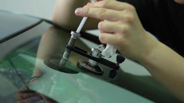 Auto glass repair 4K footage injecting polymer resin into a rock chip. Turning the injector thread on a suction cup bridge to fill a rock chip with liquid resin