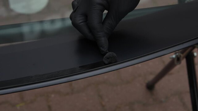 4K video of applying black primer to a new windshield edge. Mechanic applying urethane primer to the ceramic band of a new car windshield using a wool dauber