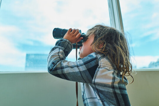Close-up of a boy looking through binoculars at a window