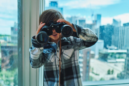 Boy peering through binoculars towards the camera with city behind