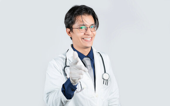 Smiling doctor pointing forward against an isolated background. Healthcare professional pointing at camera against a white background