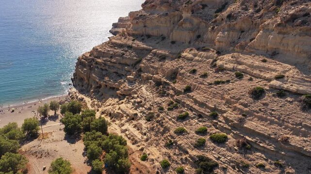 Aerial drone view of sunlight glinting on the sea beside the honeycombed cave cliff, Matala, Greece