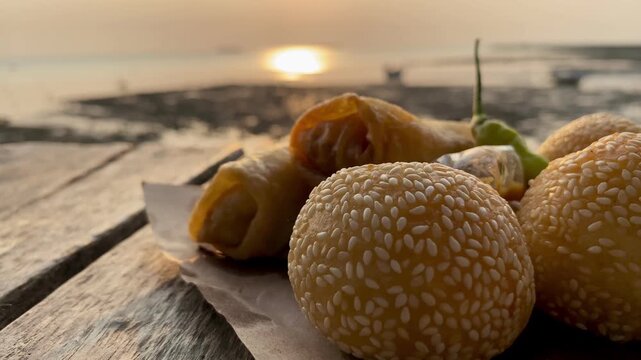 Traditional Indonesian fried snacks, sesame seed balls and crispy spring rolls on a wooden table
