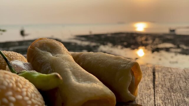 Traditional Indonesian snacks, crispy spring rolls and sesame seed balls with beach sunset view