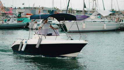 Fototapeta premium Person steering a motorboat through a busy marina in summer
