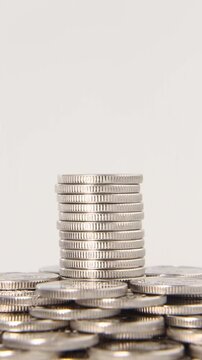 A tall neat stack of silver coins stands in the center of a pile of coins on a light gray background in a seamless loop, highlighting the concept of growth, savings and wealth. Looping video