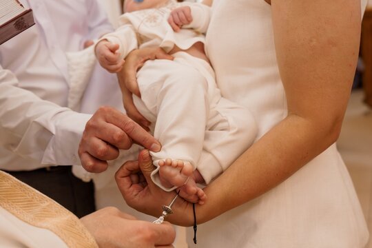 Priest anointing baby foot during baptism ceremony in church with white clothing and warm lighting.