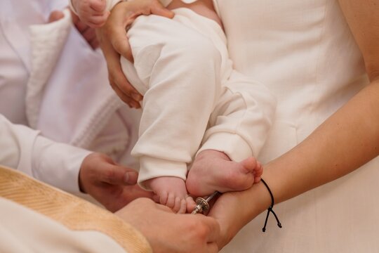 Priest anointing infant baby during a baptism ceremony in a white dress with soft neutral lighting.