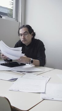 Vertical shot of a stressed male teacher frantically sorting and throwing papers on his desk in frustration