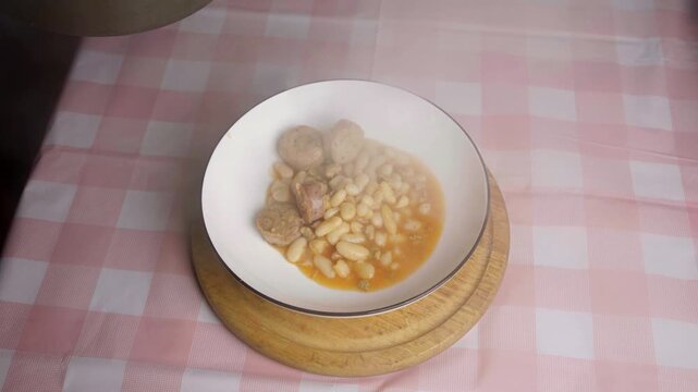 Top view of steaming white bean stew with sausages being served into a dish