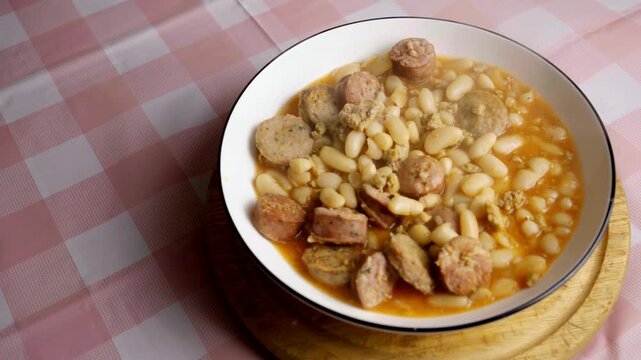 High angle shot of hot steaming white bean stew with sliced sausages in a bowl