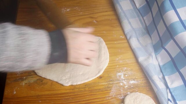 Top view of a person flattening homemade dough with a wooden rolling pin