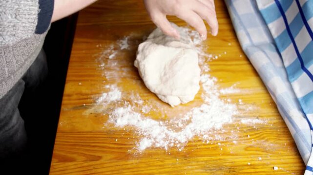 Top view of baker kneading raw pastry dough on a floured wooden table