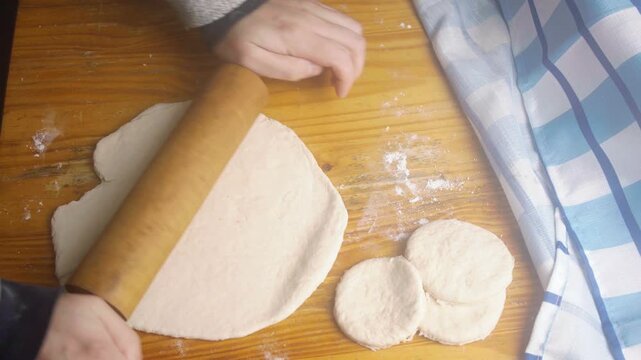 Close up of hands rolling out traditional Chilean sopaipilla dough on a wooden table