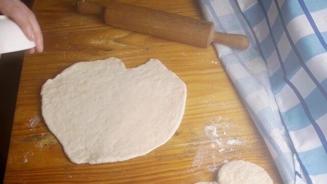Top view of baker cutting out round sopaipillas from raw dough using a small bowl