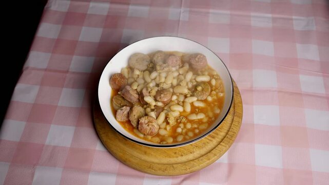 Top view of steaming white bean stew with sausages in a white bowl