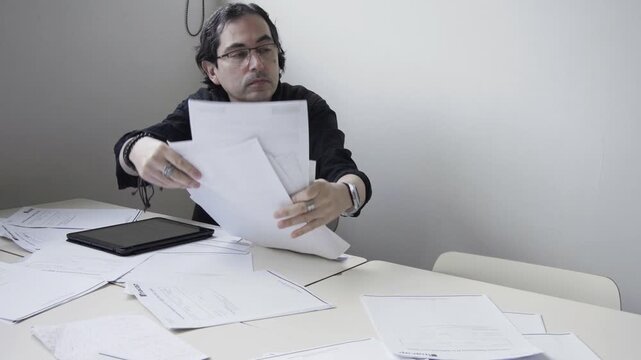 Stressed male teacher gathering and throwing papers in frustration at his desk