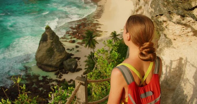 Girl looking at ocean while standing on narrow cliff path during hiking toward Diamond beach in Nusa Penida Bali
