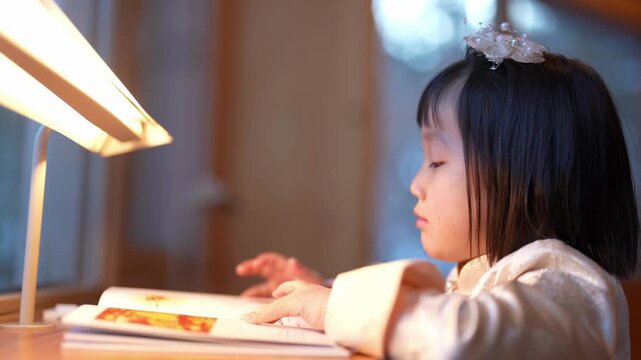Soft light glows over a quiet study scene. Child sleeps gently, eyes closed, during bedtime reading. Warm glow of desk lamp bathes her peaceful face. She wears a delicate headpiece, soft clothing