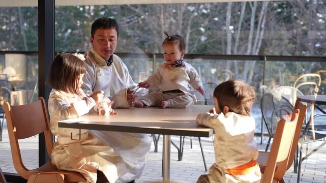 Father smiles while children play at cafe table. Bright daylight filters through glass windows. Children's laughter fills the cozy outdoor space