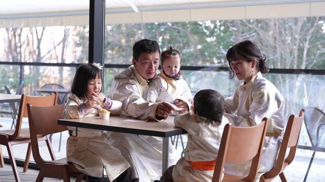 Family shares meal together at cozy restaurant. Warm smiles radiate from all seated around table. Children enjoy food with parents' gentle guidance. Ideal for family, lifestyle