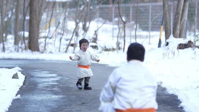 Snowy path lined with bare trees. Two children dressed warmly in white coats. One child waves happily toward the other. Children play together in winter's quiet peace. Perfect for family, seasonal