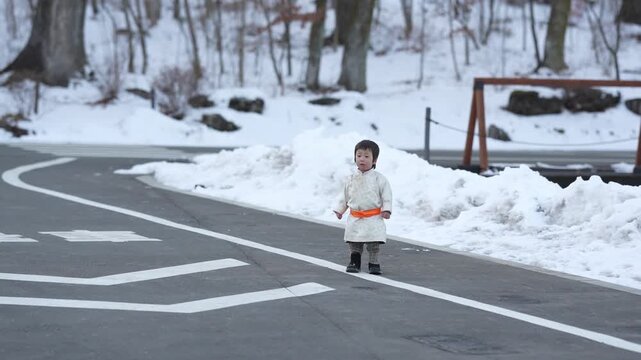 Tiny child walks snowy path. Bright coat contrasts cold winter scene. Child looks curious, unbothered by snow. Road markings guide quiet winter journey. Perfect for family, travel