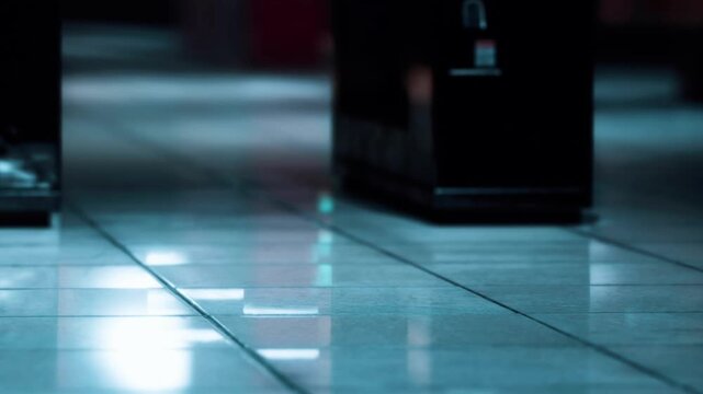 A vending machine stands alone in a dimly lit lobby. The light reflects off the floor tiles. The surroundings are quiet and empty. Shadows cast around highlight the machine.