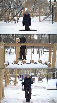 Young boy wearing winter jacket, hat and gloves plays on snowy playground. He balances on hanging wooden logs and swings on a swing set in winter park.