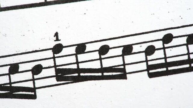Black printed piano sheet music in an extreme close-up panning shot, musical notes, staff lines, beams and fingering numbers on white paper, classical notation, sight-reading and education background