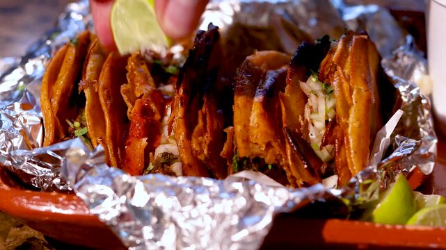 Person preparing traditional mexican birria tacos with consomm&eacute; and lime juice