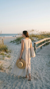 Woman walking on a sandy coastal path towards the ocean at sunset