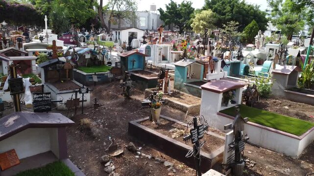 Toma de dron en desplazamiento a baja altura volando sobre un tradicional y concurrido pante&oacute;n mexicano con tumbas coloridas en Cuernavaca, M&eacute;xico.