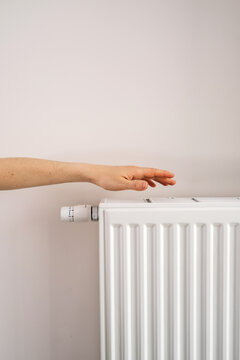 Hand reaching toward home heating radiator in modern apartment room